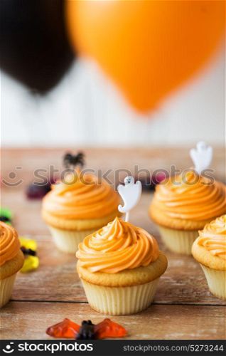 food, baking and holidays concept - cupcakes or muffins with halloween party ghost decoration on wooden table. cupcakes with halloween decoration on table