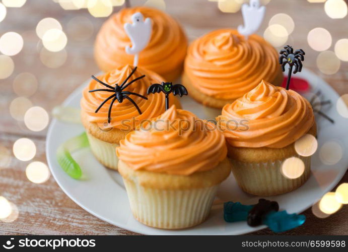 food, baking and holidays concept - cupcakes or muffins with halloween party decorations and candies on plate. halloween party decorated cupcakes on plate