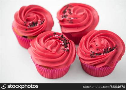 food, baking and pastry concept - close up of cupcakes or muffins with red buttercream frosting and sprinkles. close up of cupcakes with red buttercream frosting