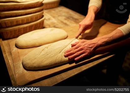 food, baking and people concept - chef or baker with knife cutting dough and cooking bread at bakery. chef or baker with dough cooking bread at bakery