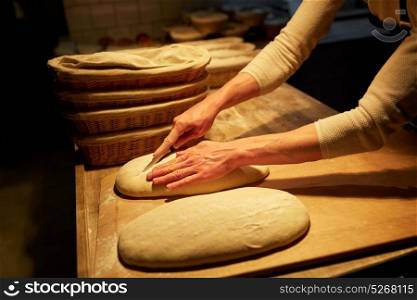 food, baking and people concept - chef or baker with knife cutting dough and cooking bread at bakery. chef or baker with dough cooking bread at bakery