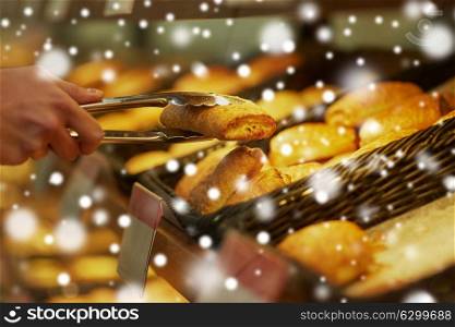 food, baking and sale concept - close up of hand with tongs taking bun at bakery or grocery store over snow. hand with tongs taking bun at bakery or grocery