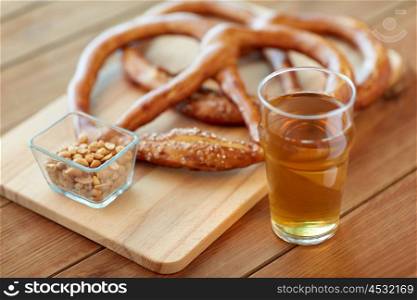 food, baking, cooking and pastry concept - close up of beer in glass, pretzels and peanuts on wooden table