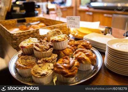 food, baking, junk-food and unhealthy eating concept - close up of butter buns or cakes on stand at cafe or bakery