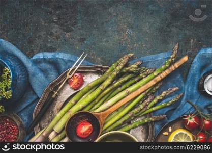 Food border with green asparagus, tomatoes,lemon and other ingredients for tasty asparagus cooking. Green asparagus preparation on dark rustic background, top view, place for text, border