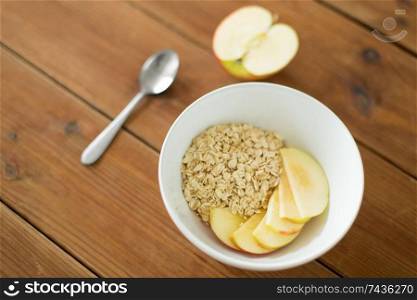 food, breakfast and healthy eating concept - oatmeal in bowl with sliced apple and spoon on wooden table. oatmeal in bowl with apple and spoon on table