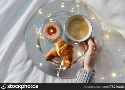 food, breakfast and people concept - hand of woman drinking coffee with croissant in bed. hand of woman drinking coffee with croissant