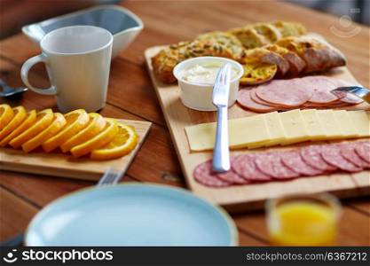 food, catering and eating concept - cream cheese with knife, sliced sausage, bread and orange on wooden table at breakfast. cream cheese and other food on table at breakfast