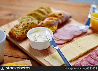 food, catering and eating concept - cream cheese with knife, sliced sausage and bread on wooden table at breakfast. cream cheese and other food on table at breakfast