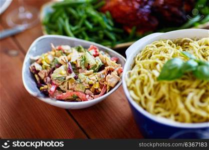 food, catering and eating concept - smoked chicken salad and pasta in bowls on wooden table. salad and pasta in bowls with other food on table