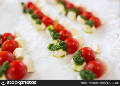 food, catering, cooking and eating concept - close up of mozzarella cheese and cherry tomato canape