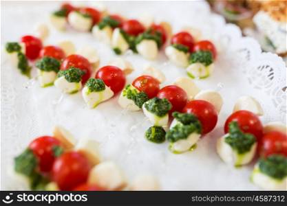 food, catering, cooking and eating concept - close up of mozzarella cheese and cherry tomato canape