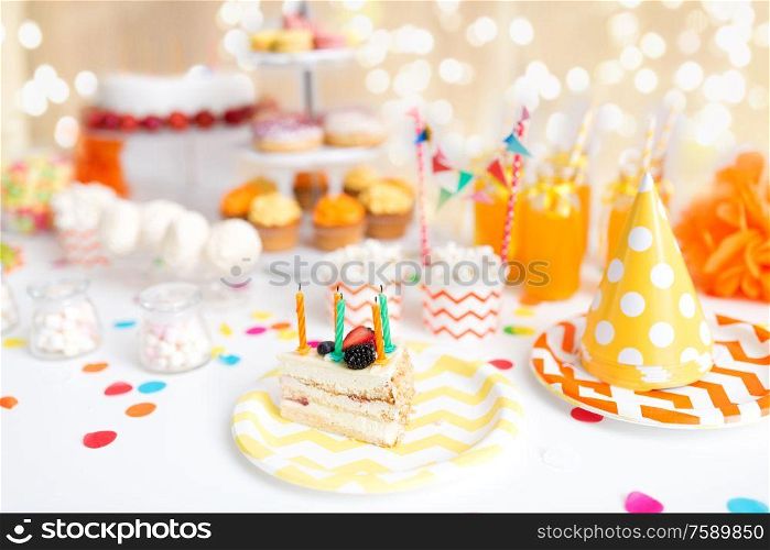 food, celebration and festive concept - piece of cake with candles on plate at birthday party over lights on beige background. piece of cake on plate at birthday party