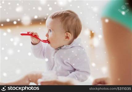 food, child, feeding and childhood concept - mother and baby with spoon eating at home over snow. mother and baby with spoon eating at home