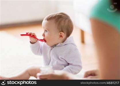 food, child, feeding and childhood concept - mother and baby with spoon eating at home