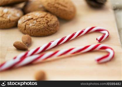 food, christmas and eating concept - close up of candy canes and oatmeal cookies with almonds on wooden board. candy canes, cookies and almonds on board