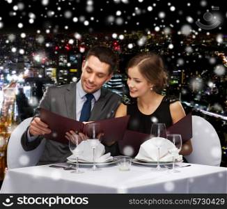 food, christmas, holidays and people concept - smiling couple with menus at restaurant over snowy night city background