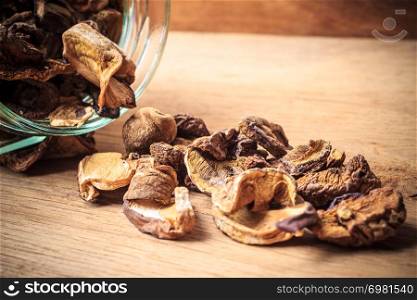 Food. Closeup dry mushrooms spilling out from storage jar on wooden surface table background.