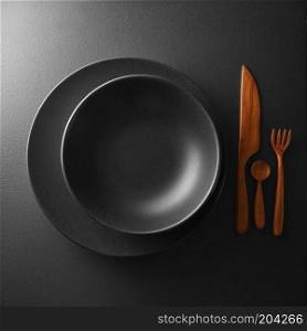 food concept - top view of black plate with knife, spoon and knife on dark table. serving of black table with dark wooden utensils and cutlery