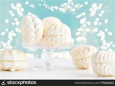 food, confection and sweets concept - close up of zephyr dessert on cake stand over lights on blue background. close up of white zephyr dessert
