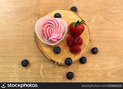 food, confection and sweets concept - zephyr, marshmallow or whipped cream with berries on wooden stand. zephyr or marshmallow with berries on stand