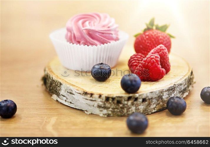 food, confection and sweets concept - zephyr, marshmallow or whipped cream with berries on wooden stand. zephyr or marshmallow with berries on stand