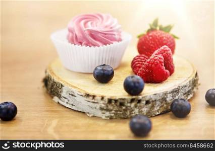 food, confection and sweets concept - zephyr, marshmallow or whipped cream with berries on wooden stand. zephyr or marshmallow with berries on stand