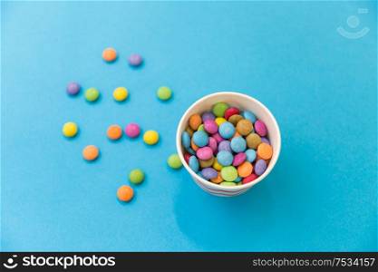 food, confectionery and sweets concept - candy drops in paper cup on blue background. candy drops in paper cup on blue background