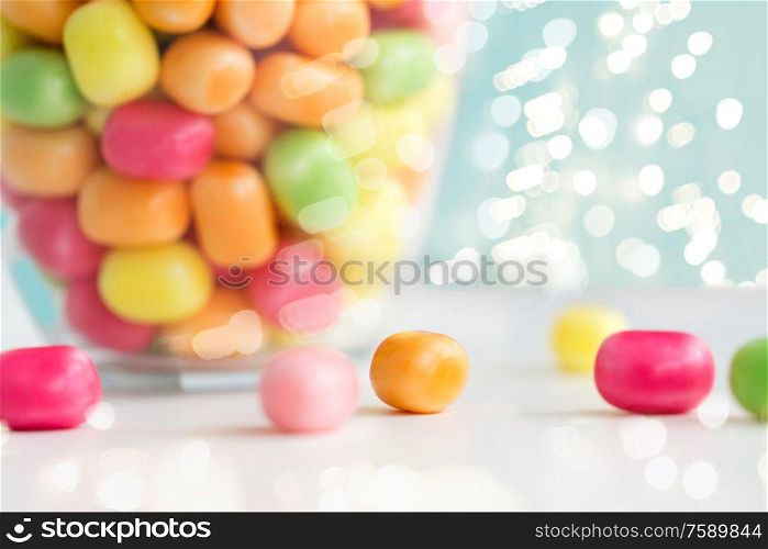 food, confectionery and sweets concept - close up of glass jar with colorful candy drops over lights on blue background. close up of colorful candy drops on table