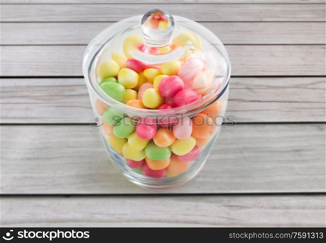 food, confectionery and sweets concept - close up of glass jar with colorful candy drops over grey wooden boards background. close up of glass jar with colorful candy drops