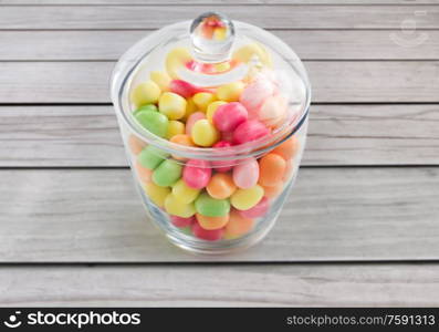 food, confectionery and sweets concept - close up of glass jar with colorful candy drops over grey wooden boards background. close up of glass jar with colorful candy drops