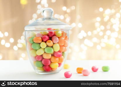 food, confectionery and sweets concept - glass jar with colorful candy drops over festive lights background. glass jar with candy drops over lights background
