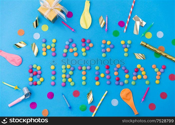food, confectionery and sweets concept - happy birthday lettering made of candy drops and party props on blue background. happy birthday of candies and party props on blue