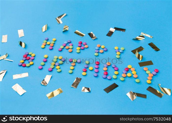 food, confectionery and sweets concept - happy birthday lettering made of candy drops and metallic confetti on blue background. happy birthday of candies and confetti on blue
