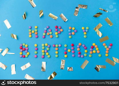 food, confectionery and sweets concept - happy birthday lettering made of candy drops and metallic confetti on blue background. happy birthday of candies and confetti on blue