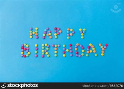 food, confectionery and sweets concept - happy birthday lettering made of candy drops on blue background. happy birthday of candy drops on blue background
