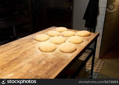 food, cooking and baking concept - yeast bread dough rising on wooden kitchen table at bakery. yeast bread dough on bakery kitchen table