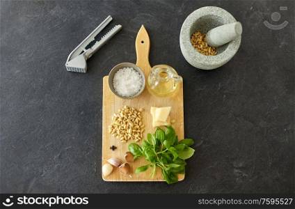 food cooking and culinary concept - mortar with pestle, parmesan cheese, pine nuts, vinegar and garlic for basil pesto sauce making on wooden cutting board. ingredients for basil pesto sauce on wooden board