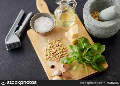 food cooking and culinary concept - parmesan cheese, pine nuts, vinegar and garlic for basil pesto sauce making on wooden cutting board. ingredients for basil pesto sauce on wooden board