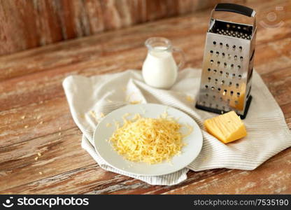 food, cooking and eating concept - close up of grated cheese, grater and jug of milk on wooden table. close up of grated cheese and jug of milk on table
