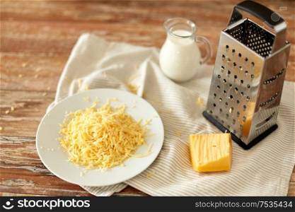 food, cooking and eating concept - close up of grated cheese, grater and jug of milk on wooden table. close up of grated cheese and jug of milk on table