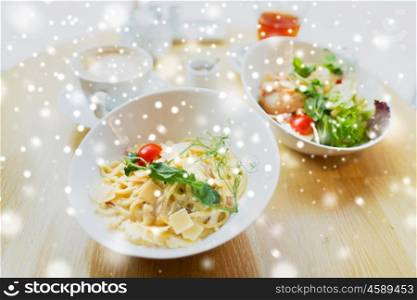 food, cooking and eating concept - close up of pasta in bowl and salad on table at restaurant or home