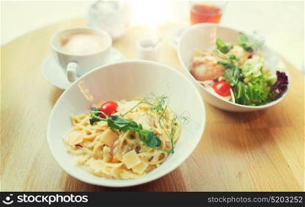 food, cooking and eating concept - close up of pasta in bowl and salad on table at restaurant or home. close up of pasta in bowl on table at restaurant