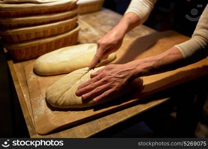food cooking, baking and people concept - baker hands making bread and cutting dough with knife at bakery. baker making bread and cutting dough at bakery