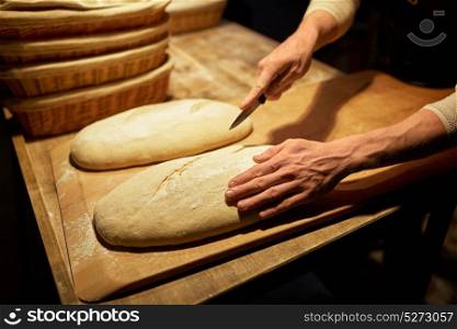 food cooking, baking and people concept - baker hands making bread and cutting dough with knife at bakery. baker making bread and cutting dough at bakery