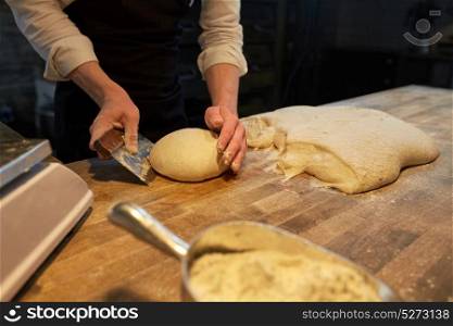 food cooking, baking and people concept - chef or baker making bread and portioning dough with bench cutter at bakery. baker portioning dough with bench cutter at bakery
