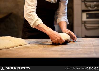 food cooking, baking and people concept - chef or baker making bread and portioning dough with bench cutter at bakery. baker portioning dough with bench cutter at bakery