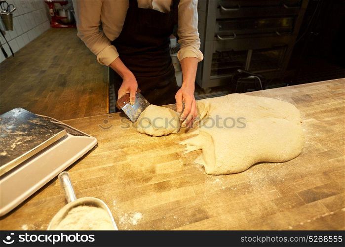 food cooking, baking and people concept - chef or baker portioning dough with bench cutter at bakery. baker portioning dough with bench cutter at bakery