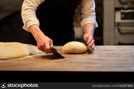 food cooking, baking and people concept - chef or baker portioning dough with bench cutter at bakery (motion blurred picture). baker portioning dough with bench cutter at bakery