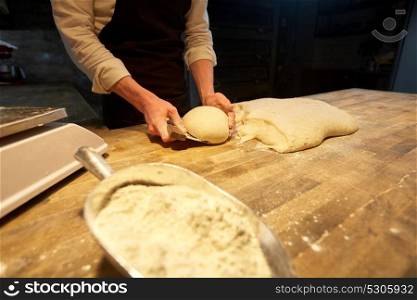 food cooking, baking and people concept - chef or baker portioning dough with bench cutter at bakery. baker portioning dough with bench cutter at bakery